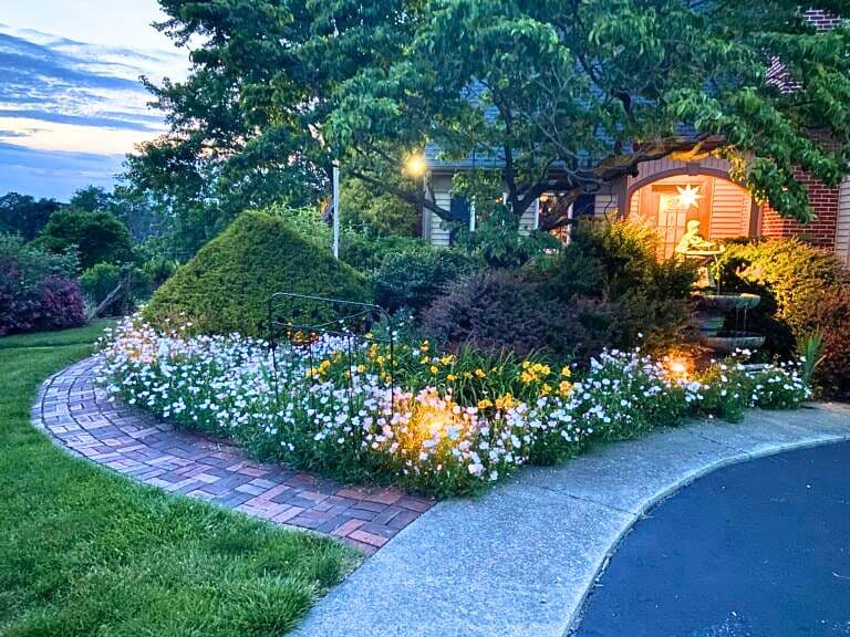 A charming garden path lined with blooming flowers and soft evening lighting leading to a house.