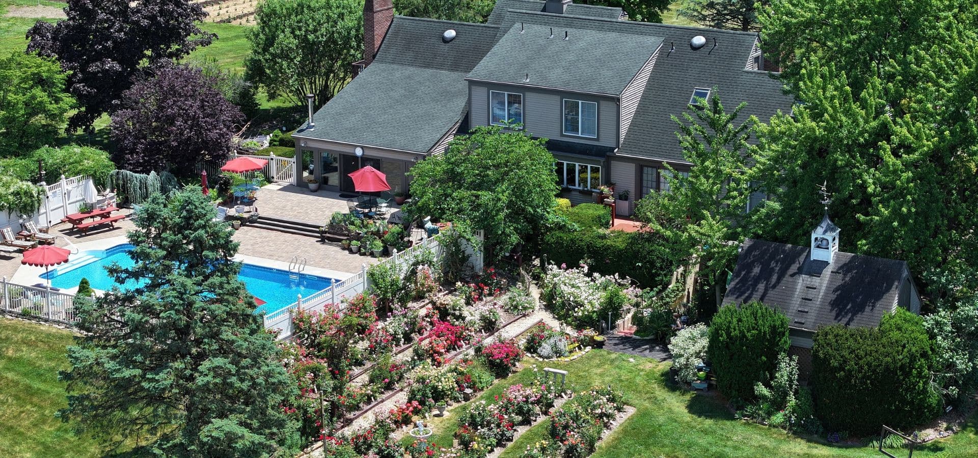 Aerial view of a house with a pool and vibrant garden in a lush landscape.
